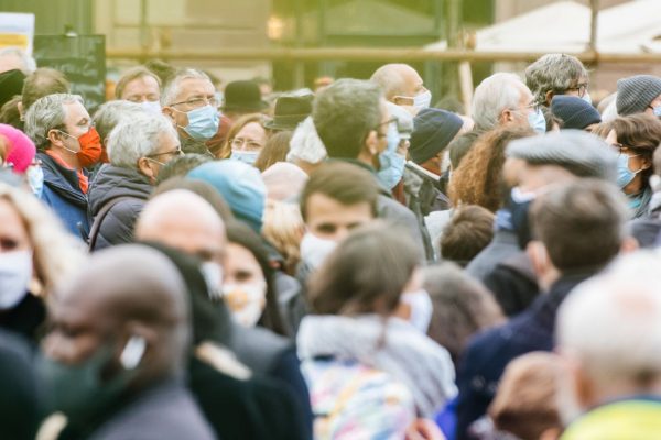 People walk along a crowded sidewalk wearing surgical masks
