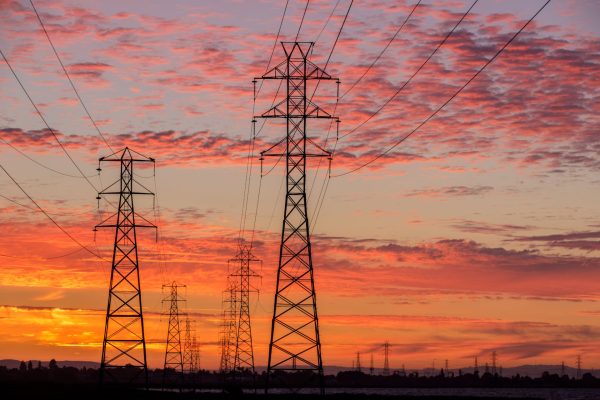 High voltage power lines stretch between pylon towers at sunset