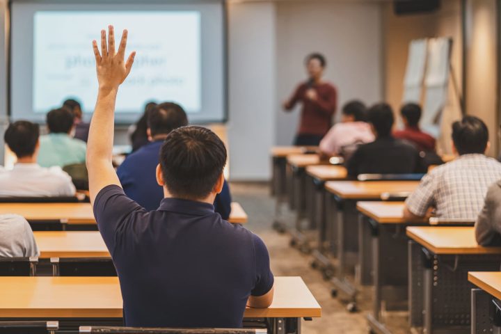 Rear view of a person raising their hand during a presentation in a classroom